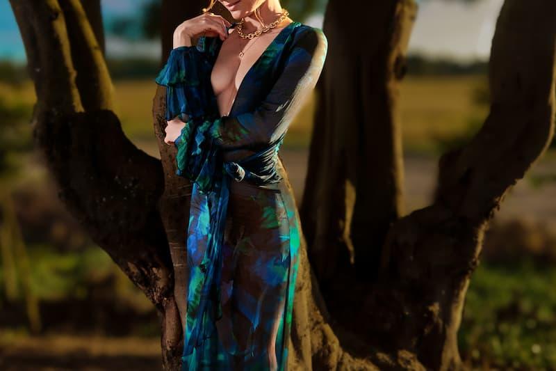High-class escort in Brasschaat wearing a plunging blue and green floral gown with a gold chain necklace at sunset